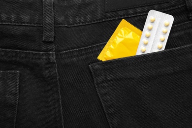 Photo of Closeup view of jeans with yellow condom and birth control pills in pocket. Safe sex concept