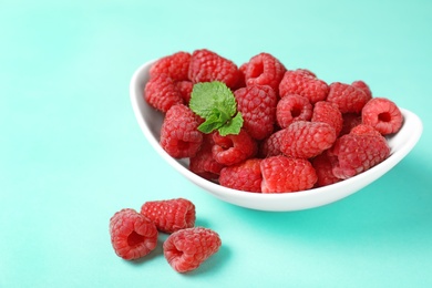 Bowl of delicious ripe raspberries on turquoise background