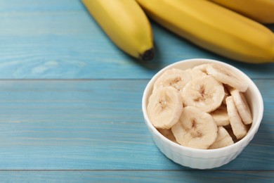 Photo of Bowl with cut bananas near whole fruits on light blue wooden table. Space for text