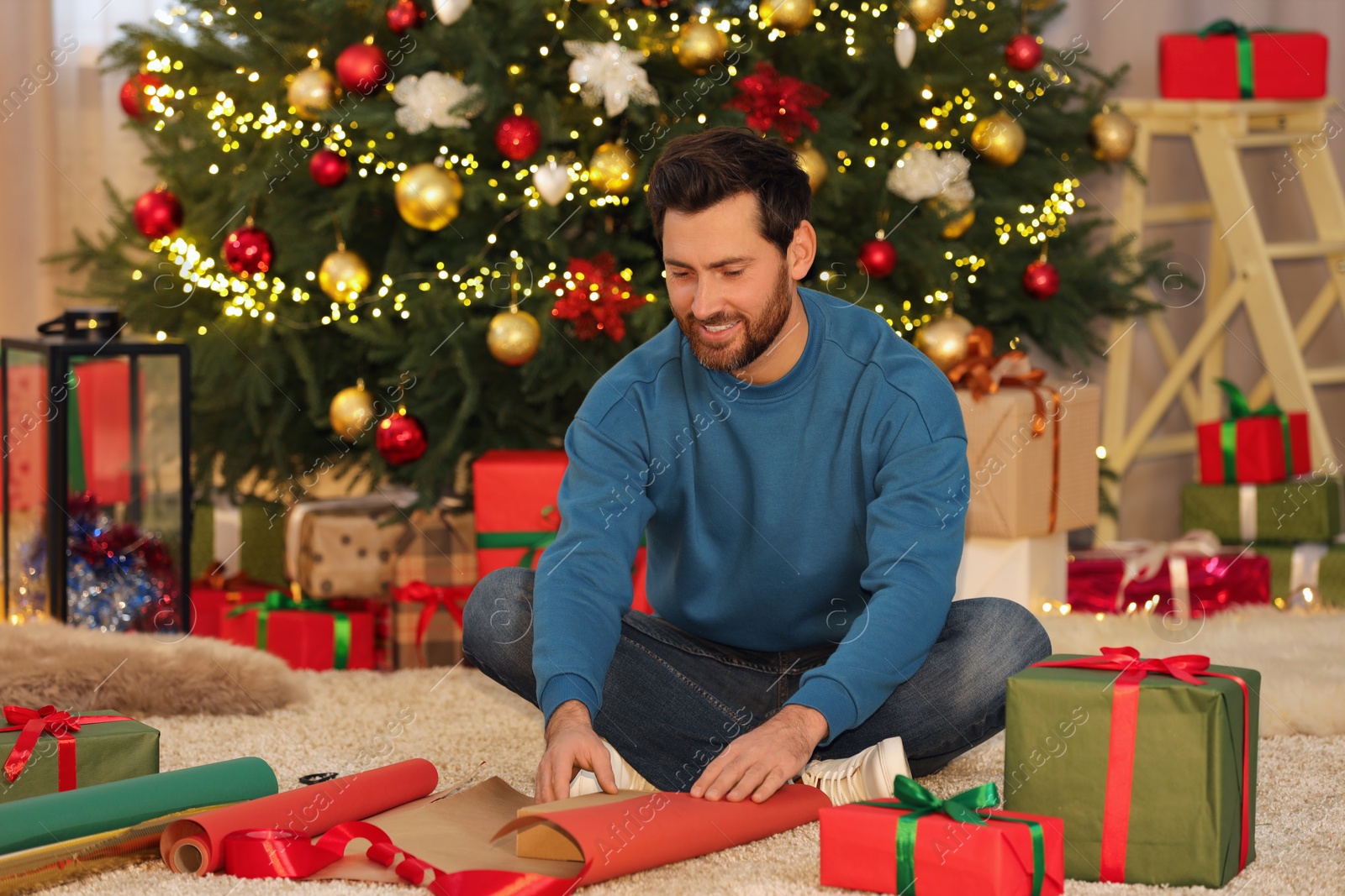 Photo of Happy man decorating Christmas gift with wrapping paper at home
