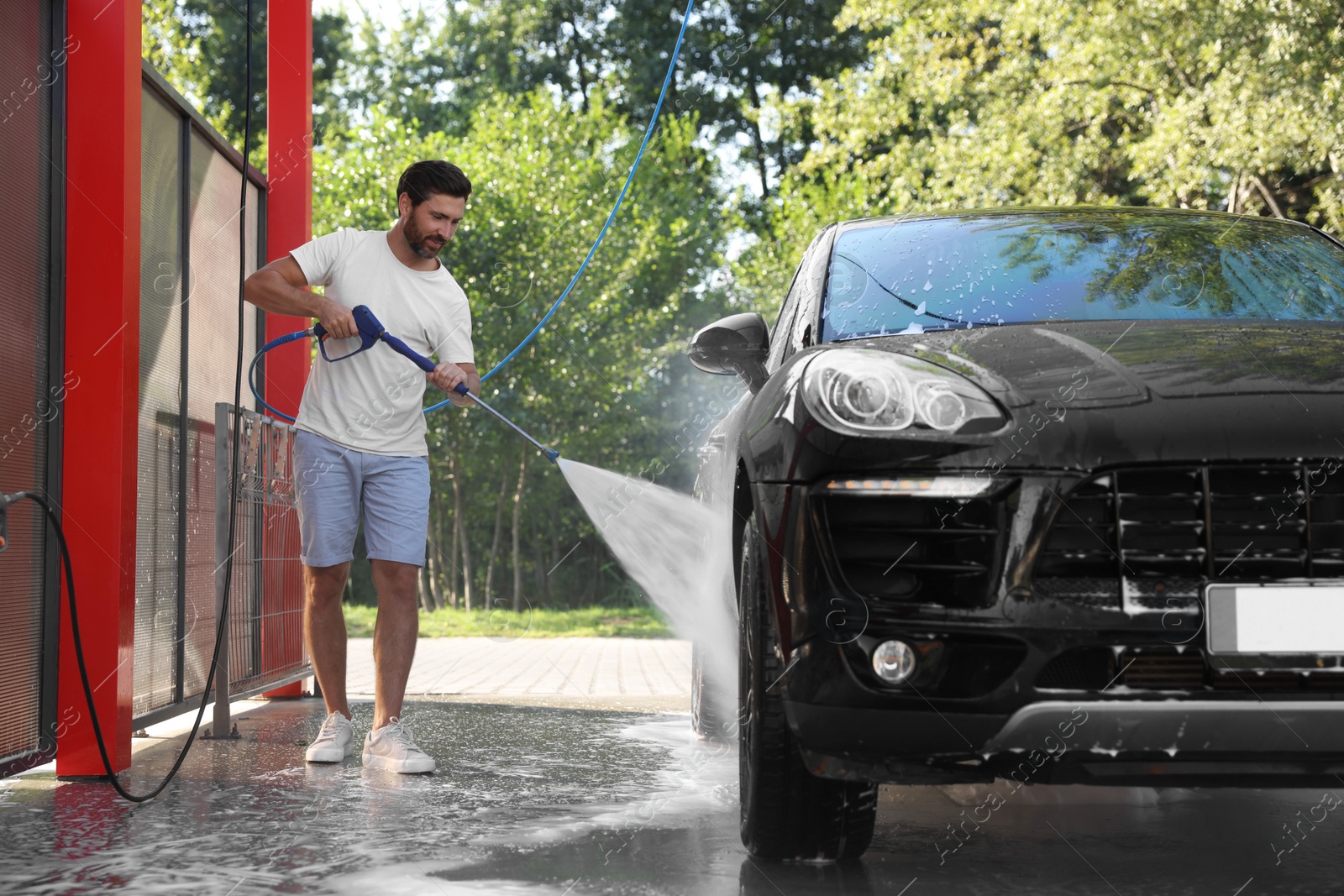 Photo of Happy man washing auto with high pressure water jet at outdoor car wash