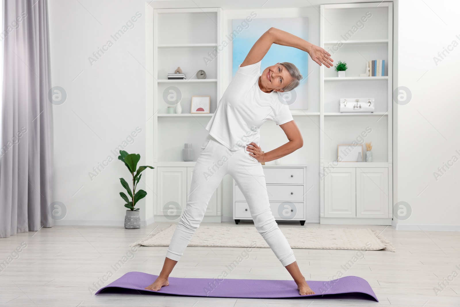 Photo of Happy senior woman practicing yoga on mat at home