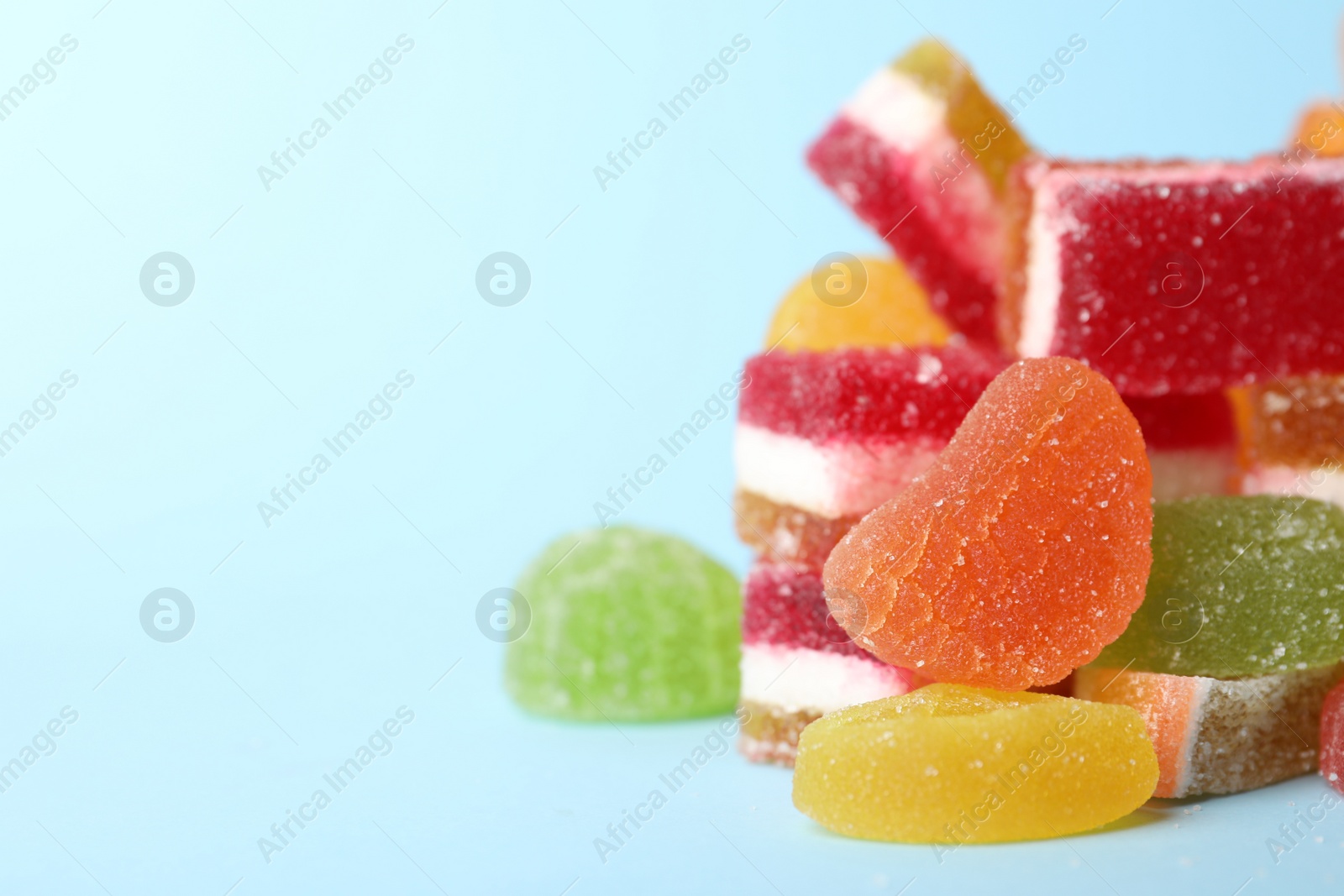 Photo of Pile of delicious bright jelly candies on light blue background, closeup. Space for text