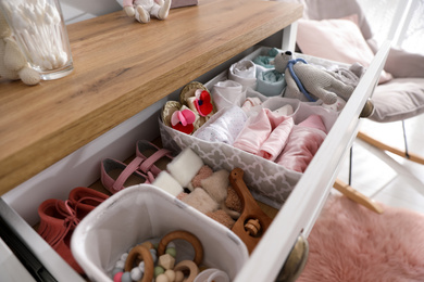 Photo of Modern open chest of drawers with baby clothes and accessories in room