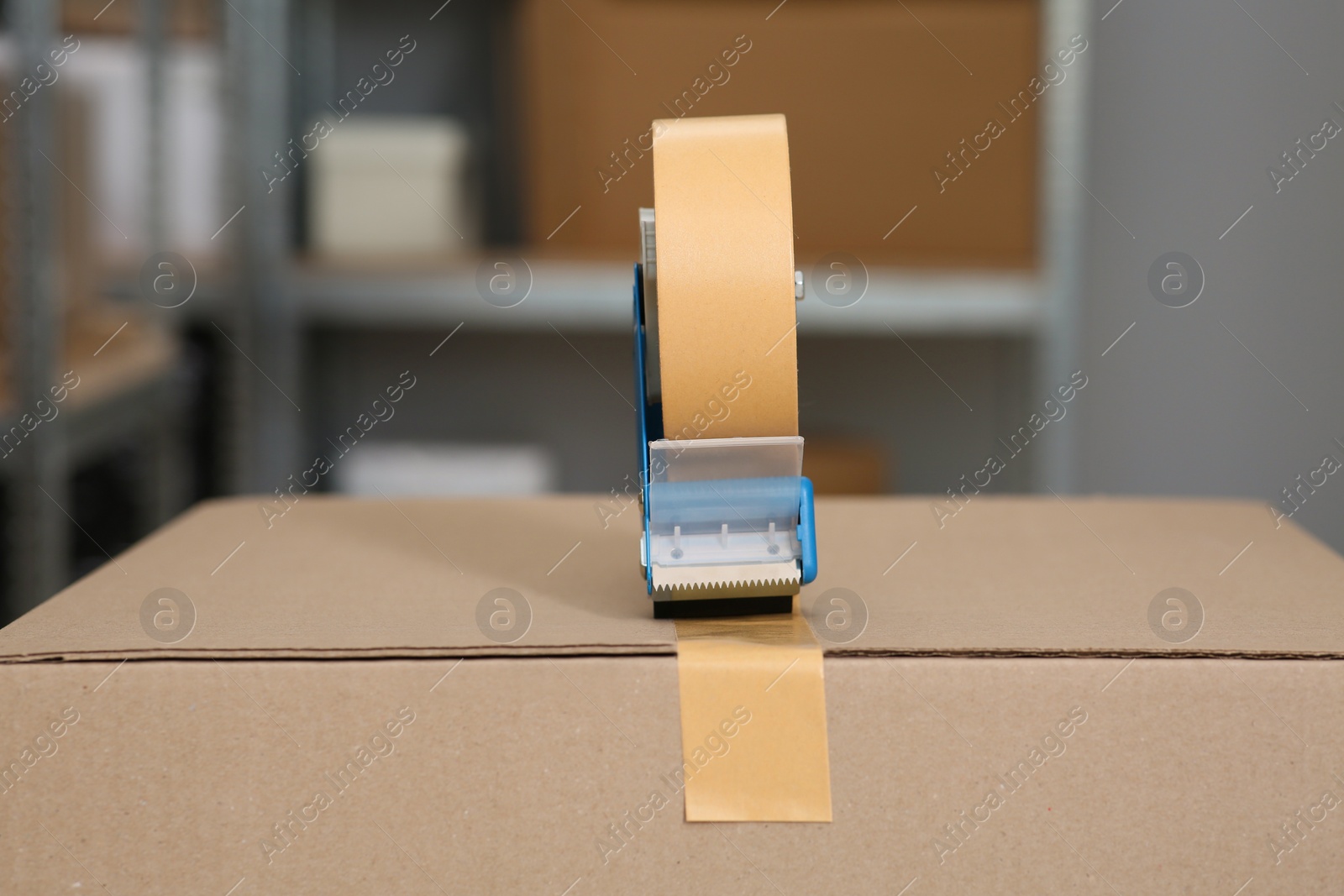 Photo of Taping cardboard box with adhesive tape dispenser indoors