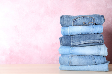 Photo of Stack of different jeans on wooden table against pink background. Space for text