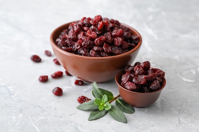 Photo of Tasty dried cranberries and leaves in bowls on grey table