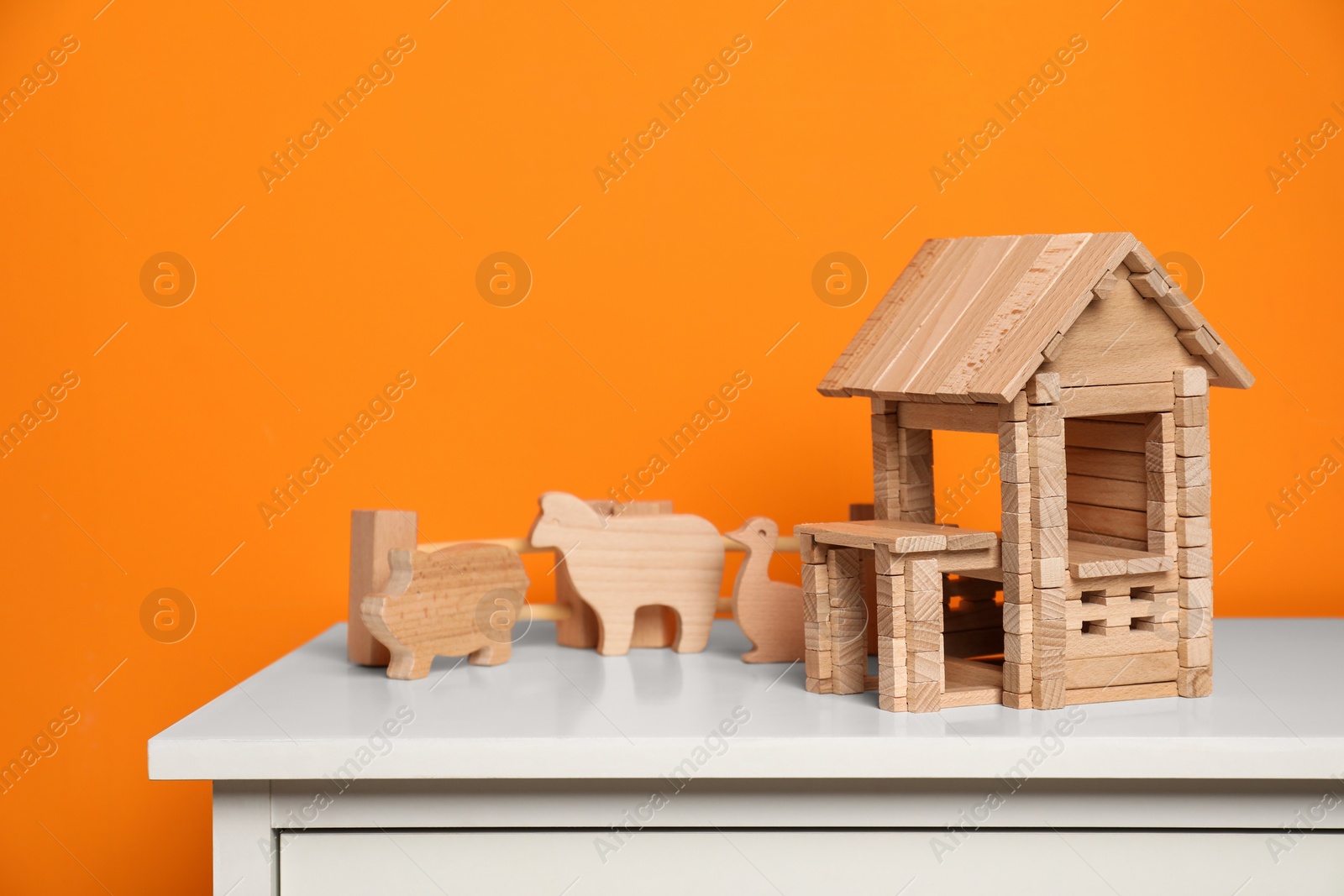 Photo of Wooden house, animals and fence on white chest of drawers near orange wall. Children's toys