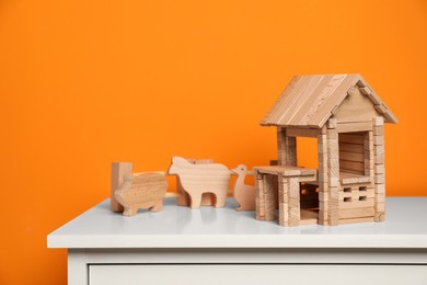 Photo of Wooden house, animals and fence on white chest of drawers near orange wall. Children's toys