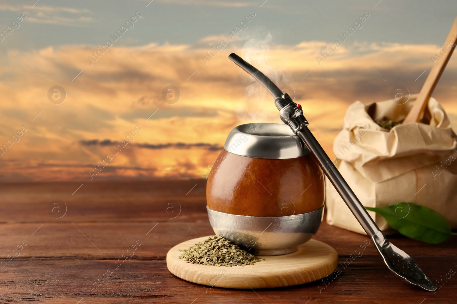 Image of Calabash with mate tea and bombilla on wooden table outdoors at sunset. Space for text