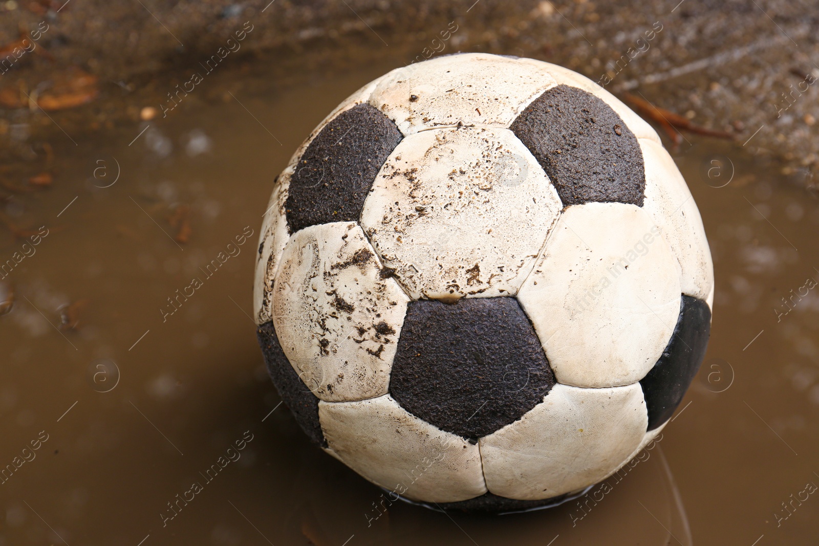 Photo of Dirty soccer ball in muddy puddle, closeup