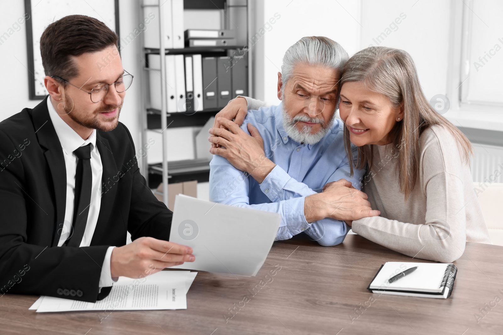 Photo of Elderly couple consulting insurance agent about pension plan at wooden table indoors