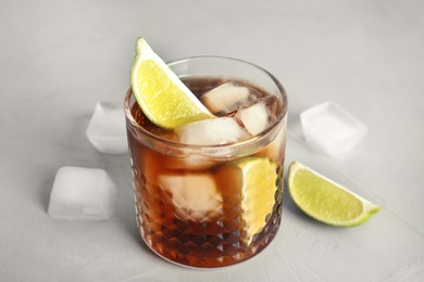 Photo of Glass of cocktail with cola, ice and cut lime on light background