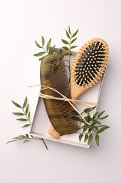 Photo of Wooden hairbrush, comb and green leaves on white background, top view