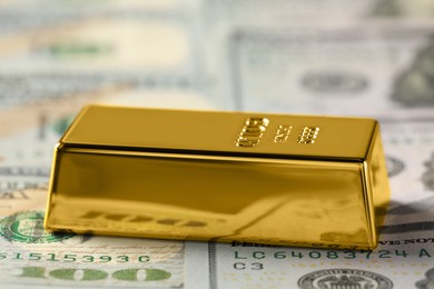 Photo of Shiny gold bar on dollar banknotes, closeup