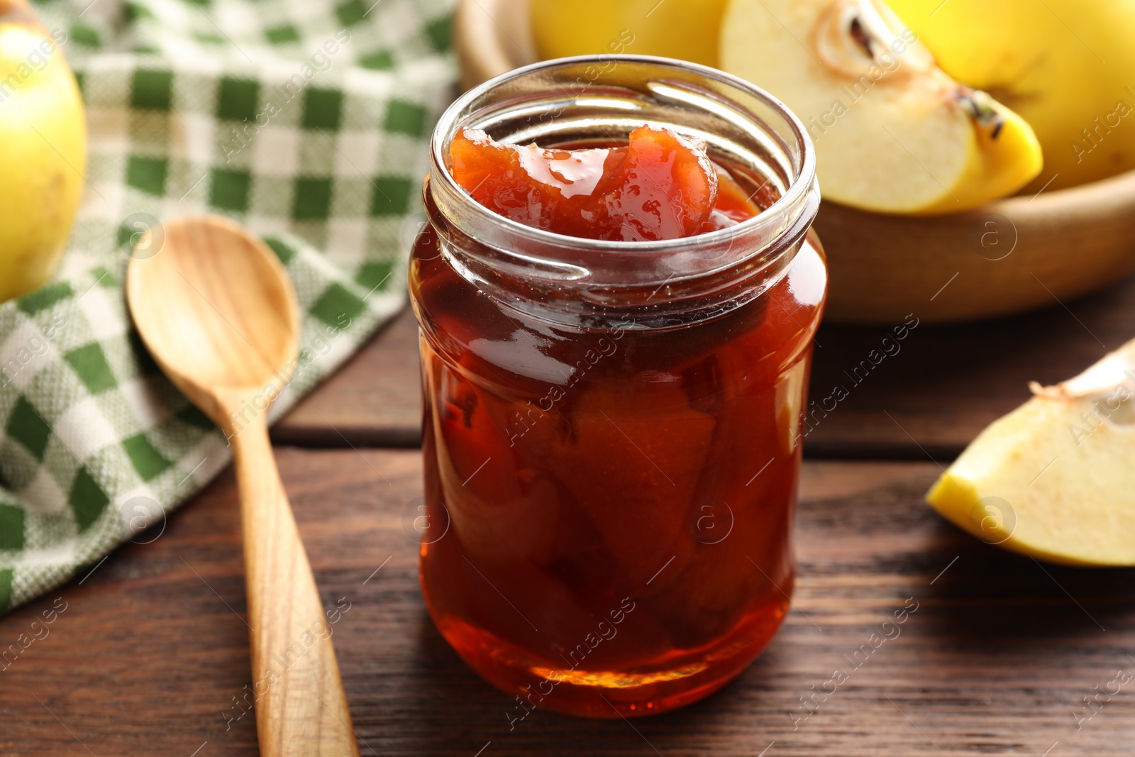 Photo of Tasty homemade quince jam in jar, spoon and fruits on wooden table, closeup