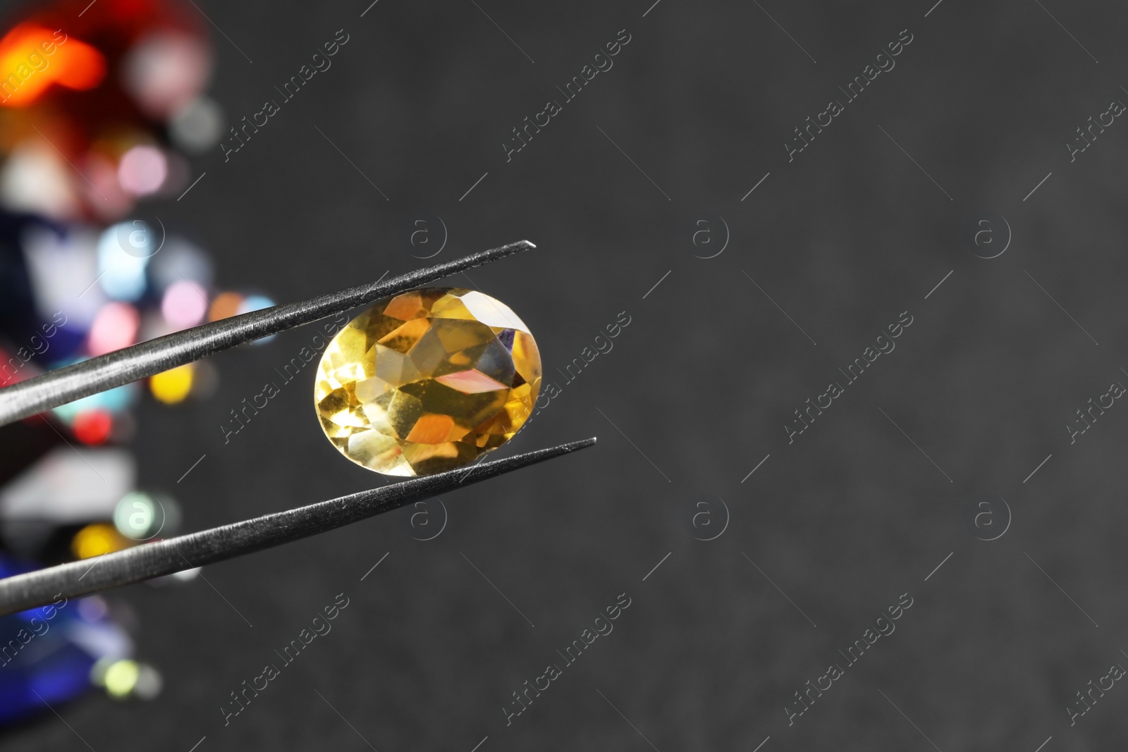 Photo of Tweezers with beautiful gemstone on blurred background. Space for text