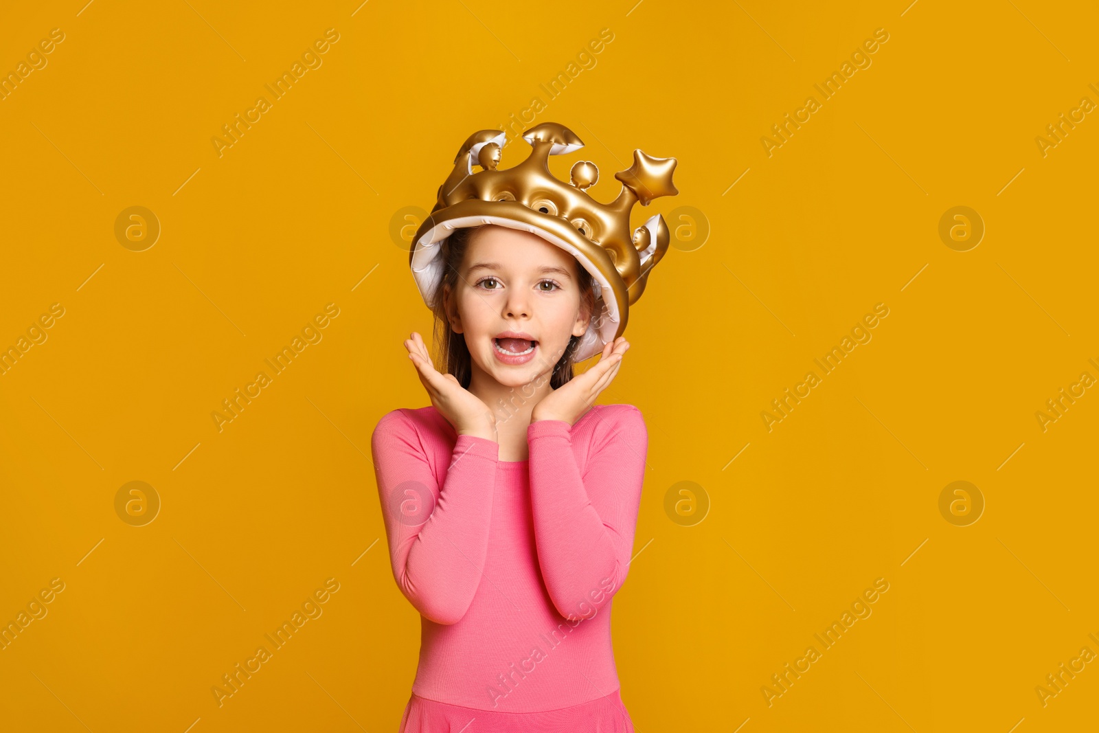 Photo of Cute girl in inflatable crown on yellow background. Little princess