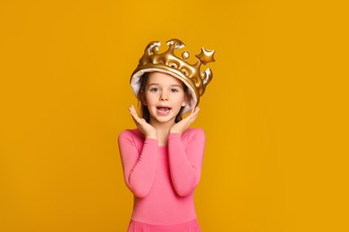 Photo of Cute girl in inflatable crown on yellow background. Little princess