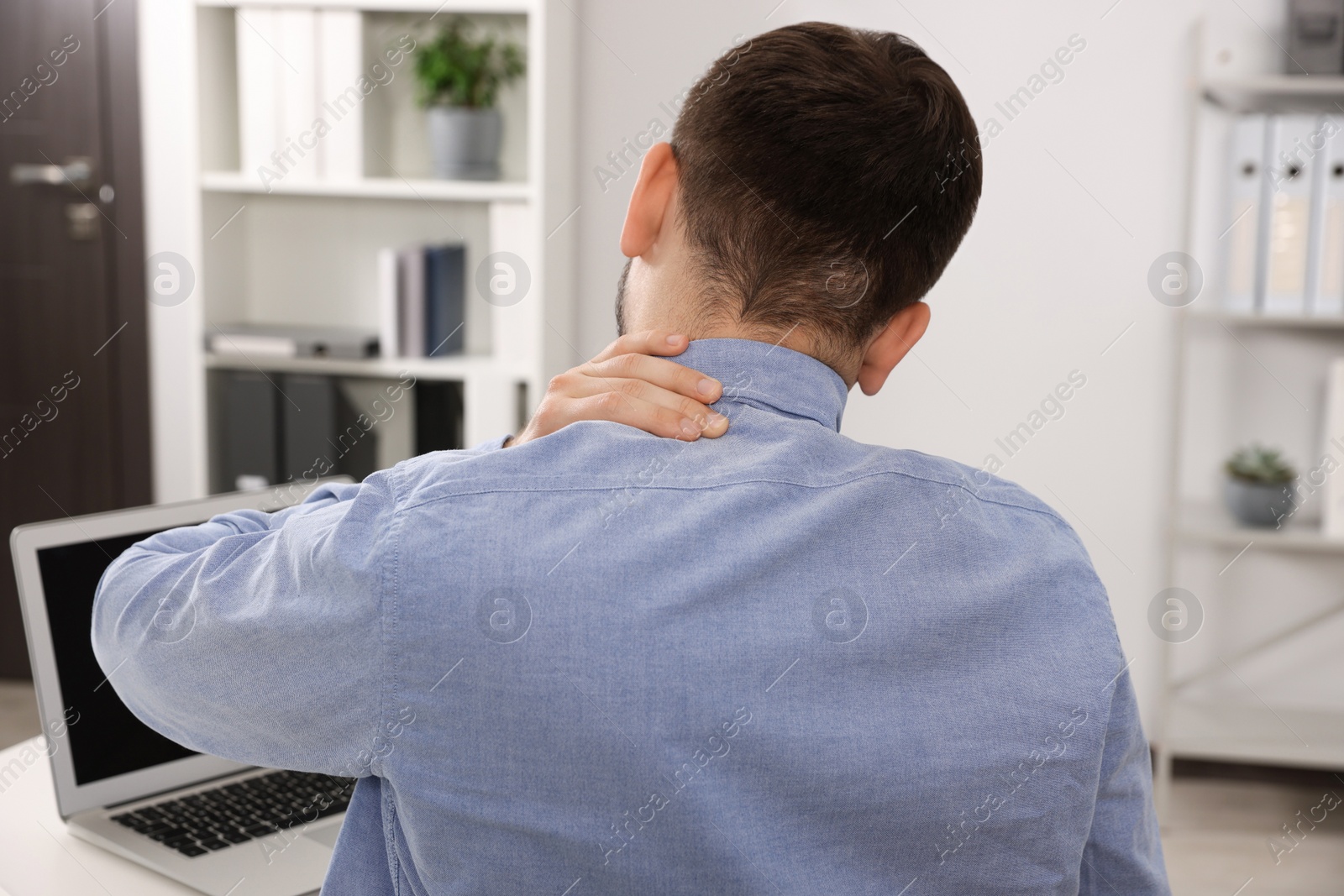 Photo of Man suffering from neck pain in office, back view