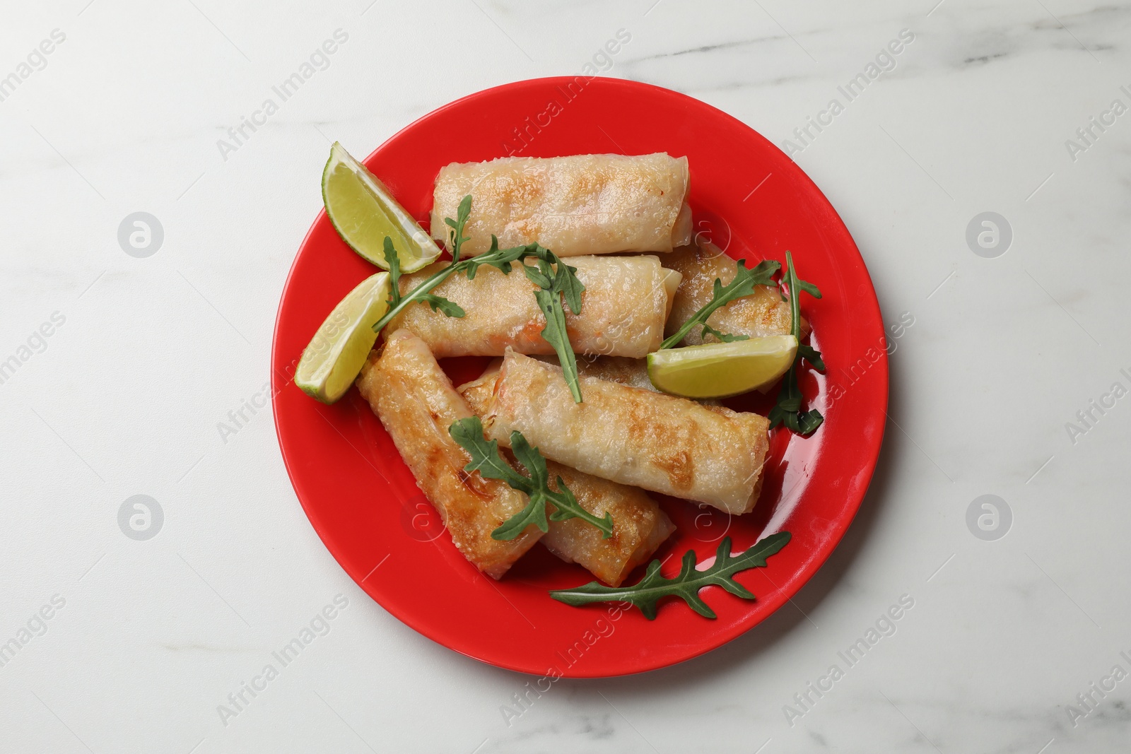 Photo of Plate with tasty fried spring rolls, arugula and lime on white table, top view