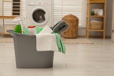 Different cleaning products in bucket on floor indoors, space for text