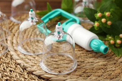 Photo of Cupping therapy. Plastic cups and hand pump on wicker mat, closeup