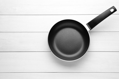 Photo of New non-stick frying pan on white wooden table, top view. Space for text