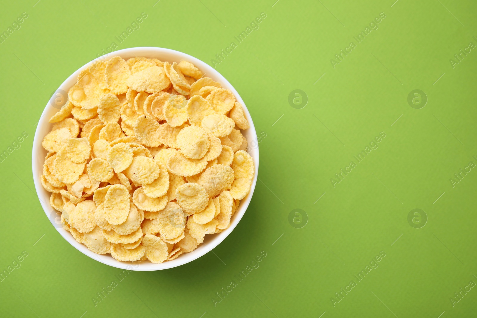 Photo of Breakfast cereal. Tasty corn flakes in bowl on green table, top view. Space for text