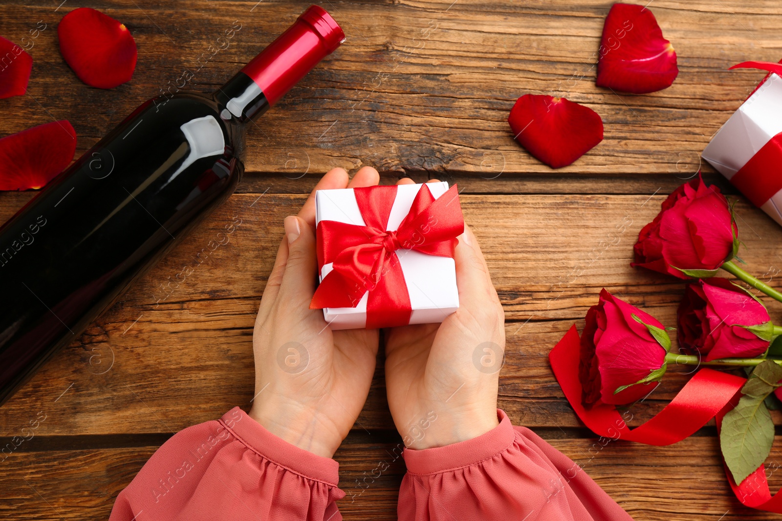 Photo of Woman holding beautiful gift box at wooden table, top view. Valentine's Day celebration