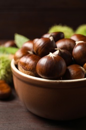 Photo of Fresh sweet edible chestnuts on brown wooden table, closeup