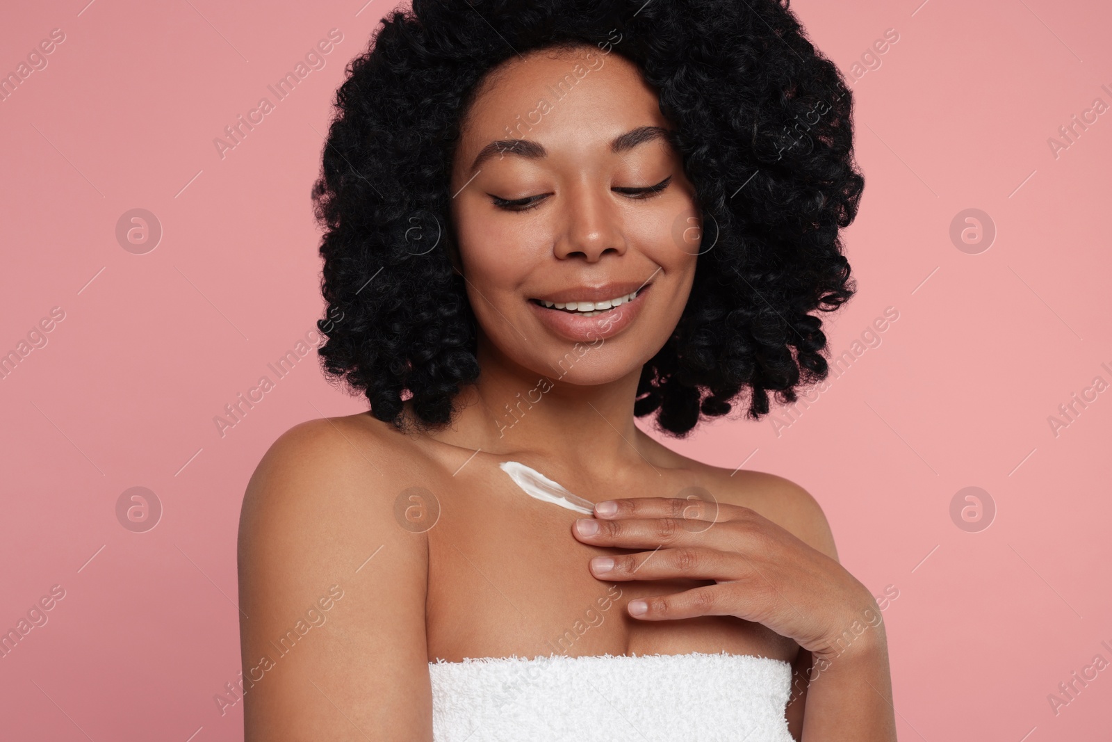 Photo of Young woman applying cream onto body on pink background