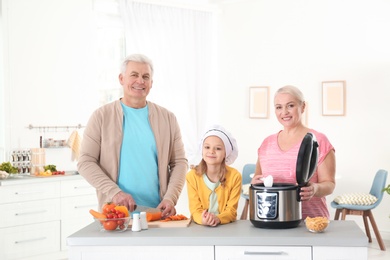 Mature couple and their granddaughter preparing food with modern multi cooker in kitchen