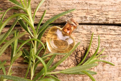 Aromatic essential oil in bottle and rosemary on wooden table, flat lay