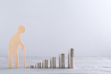 Pension savings. Figure of senior man and stacked coins on grey wooden table, space for text