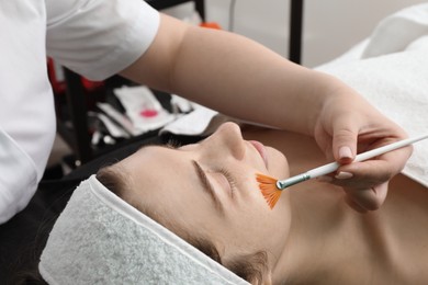 Photo of Cosmetologist with brush applying cosmetic product to client`s face in clinic, closeup