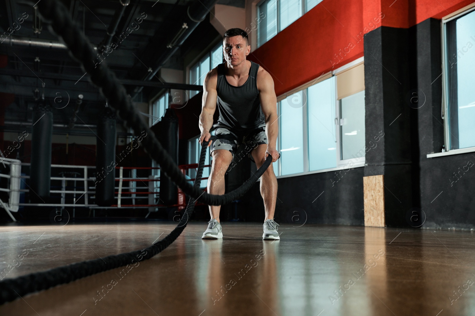 Photo of Man working out with battle ropes in modern gym