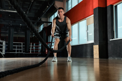 Photo of Man working out with battle ropes in modern gym
