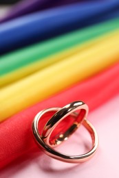 Photo of Rainbow LGBT flag and wedding rings on pink background, closeup