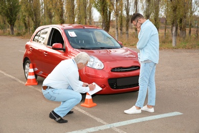 Photo of Senior instructor and man near car outdoors. Passing driving license exam