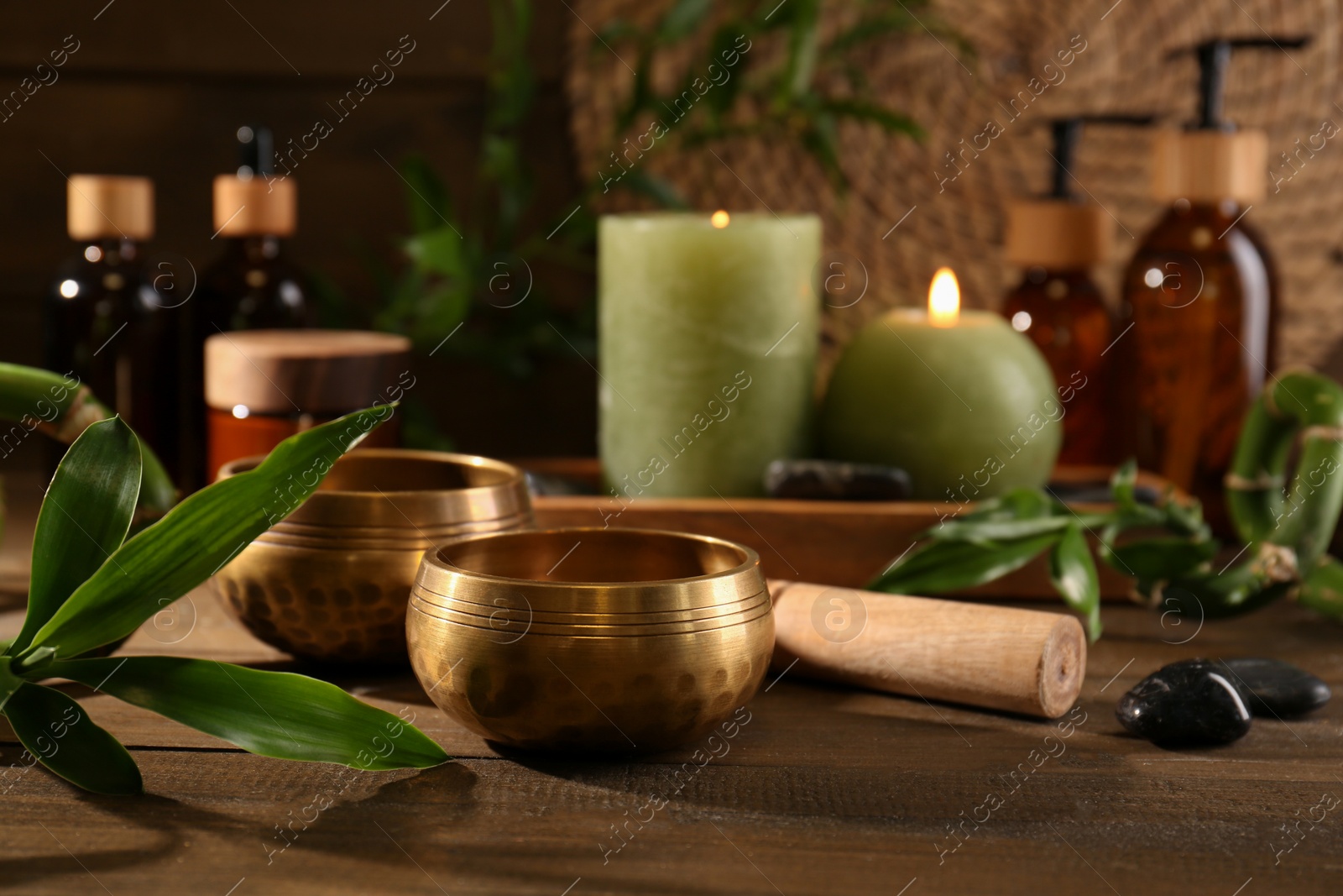 Photo of Green branches, singing bowls and burning candles on wooden table