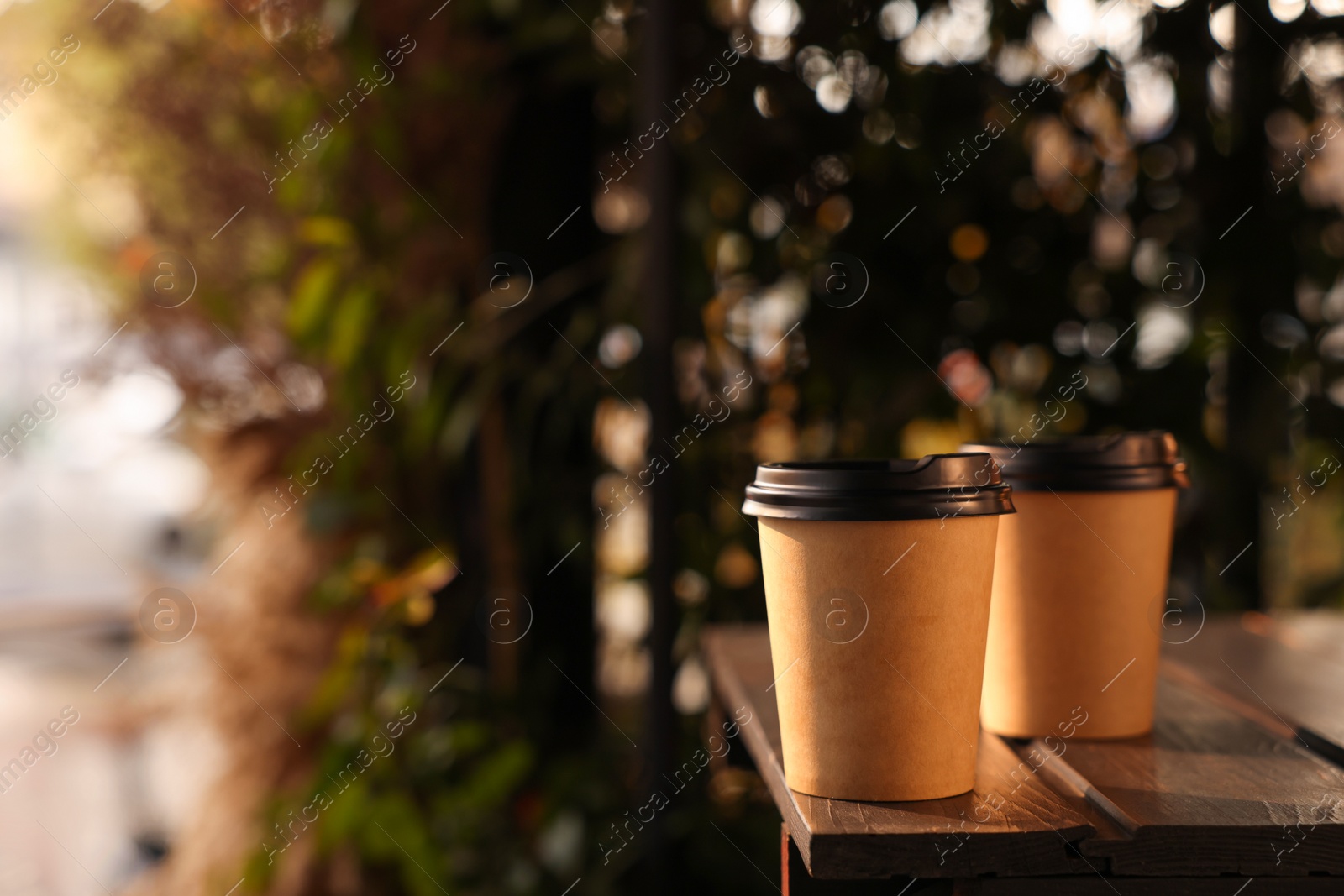 Photo of Paper coffee cups on wooden table outdoors. Space for text