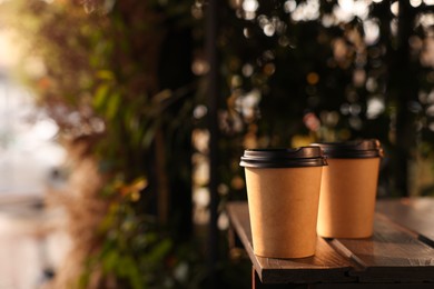 Paper coffee cups on wooden table outdoors. Space for text