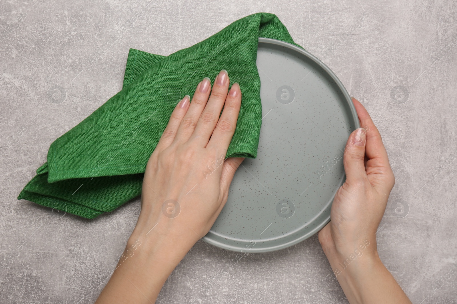 Photo of Woman wiping plate at light grey table, top view