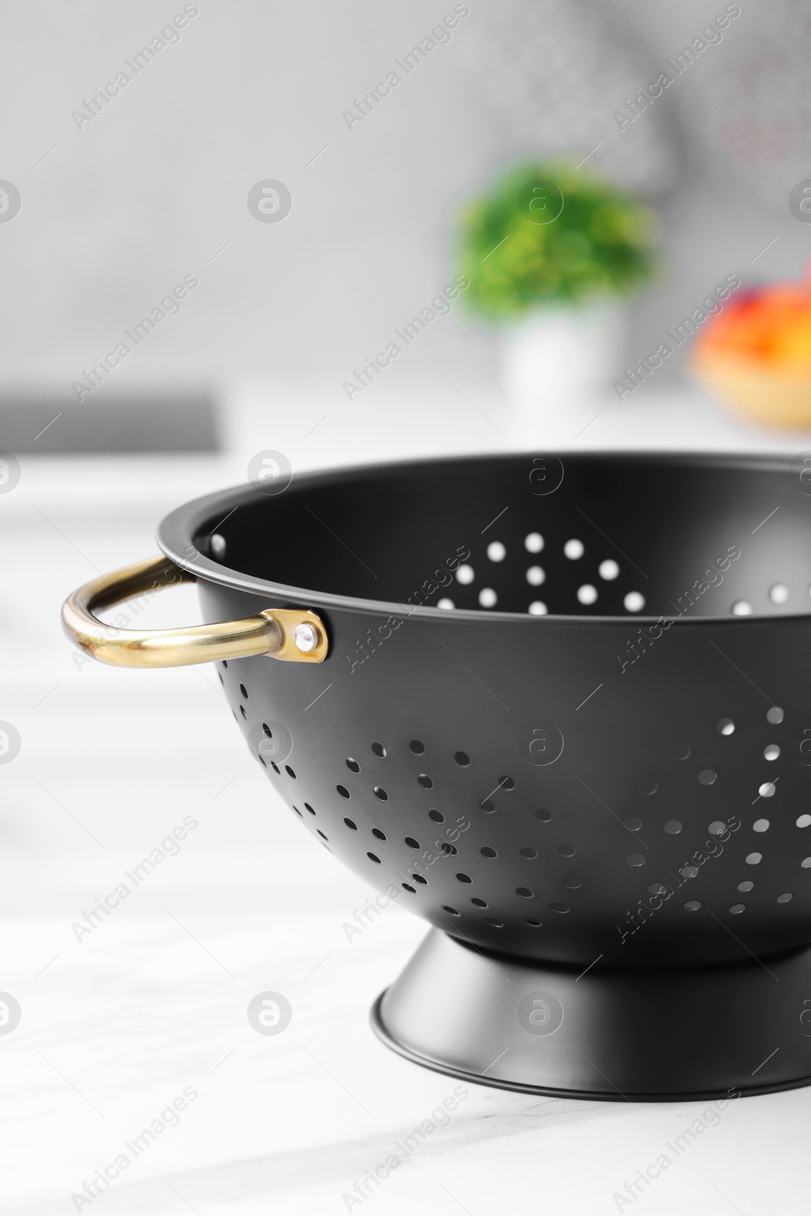 Photo of Black colander on white marble table in kitchen, closeup