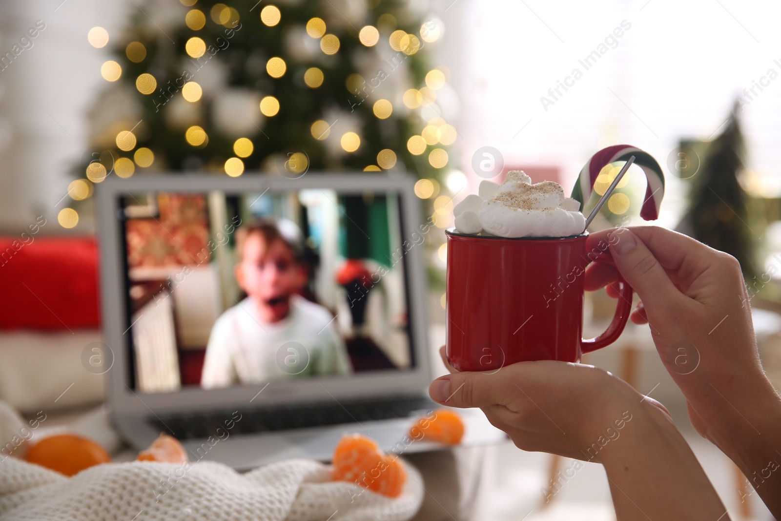 Photo of MYKOLAIV, UKRAINE - DECEMBER 25, 2020: Woman with sweet drink watching Home Alone movie on laptop indoors, closeup. Cozy winter holidays atmosphere