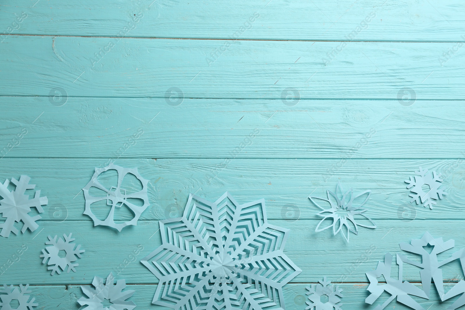 Photo of Many paper snowflakes on turquoise wooden background, flat lay. Space for text