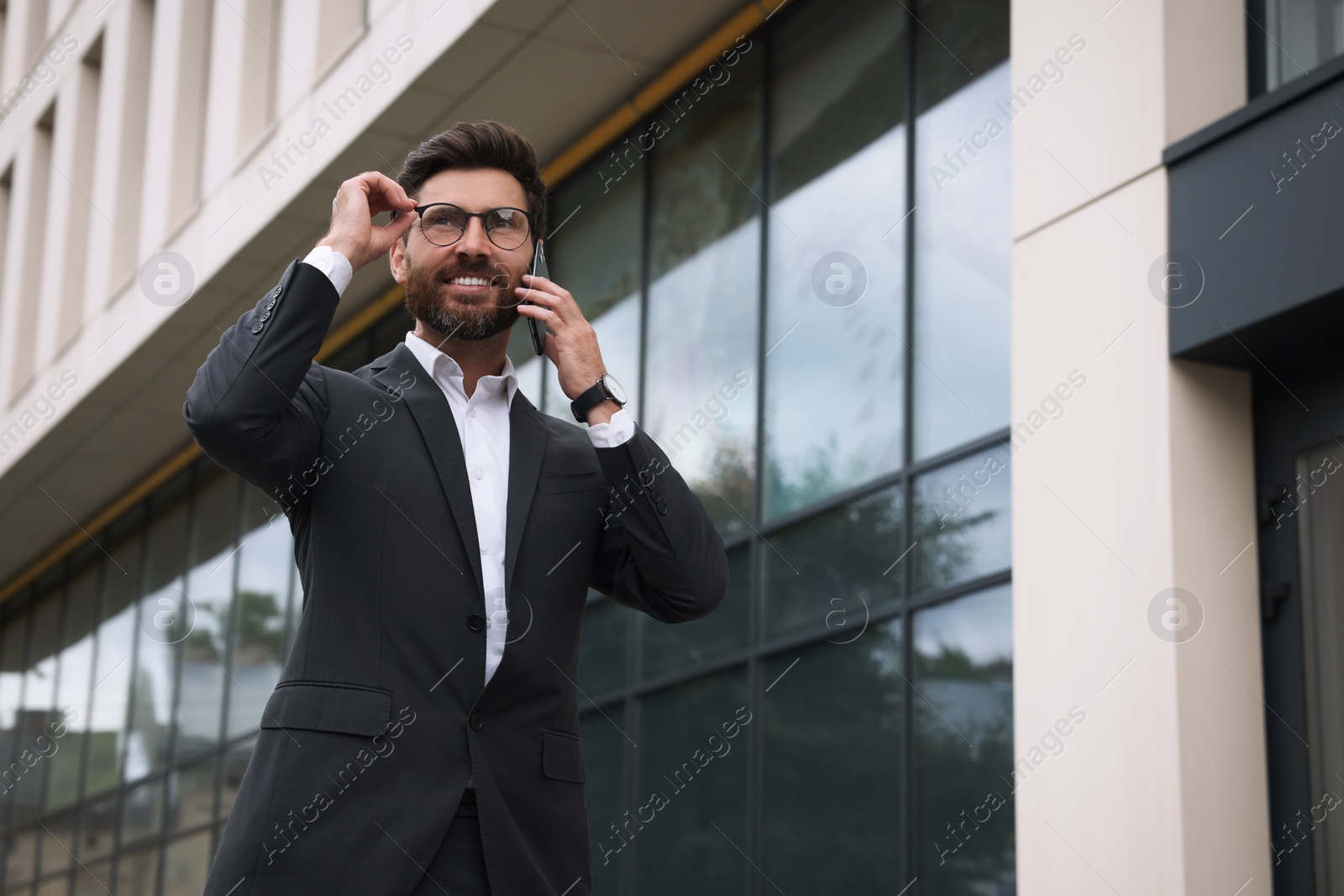 Photo of Handsome businessman talking on smartphone while walking outdoors, space for text