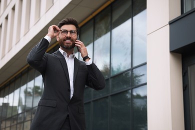 Photo of Handsome businessman talking on smartphone while walking outdoors, space for text