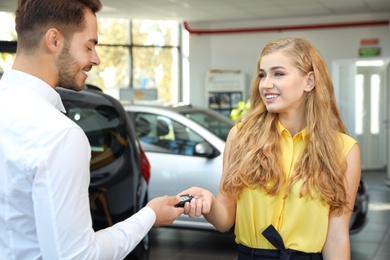 Young salesman giving car key to client in dealership